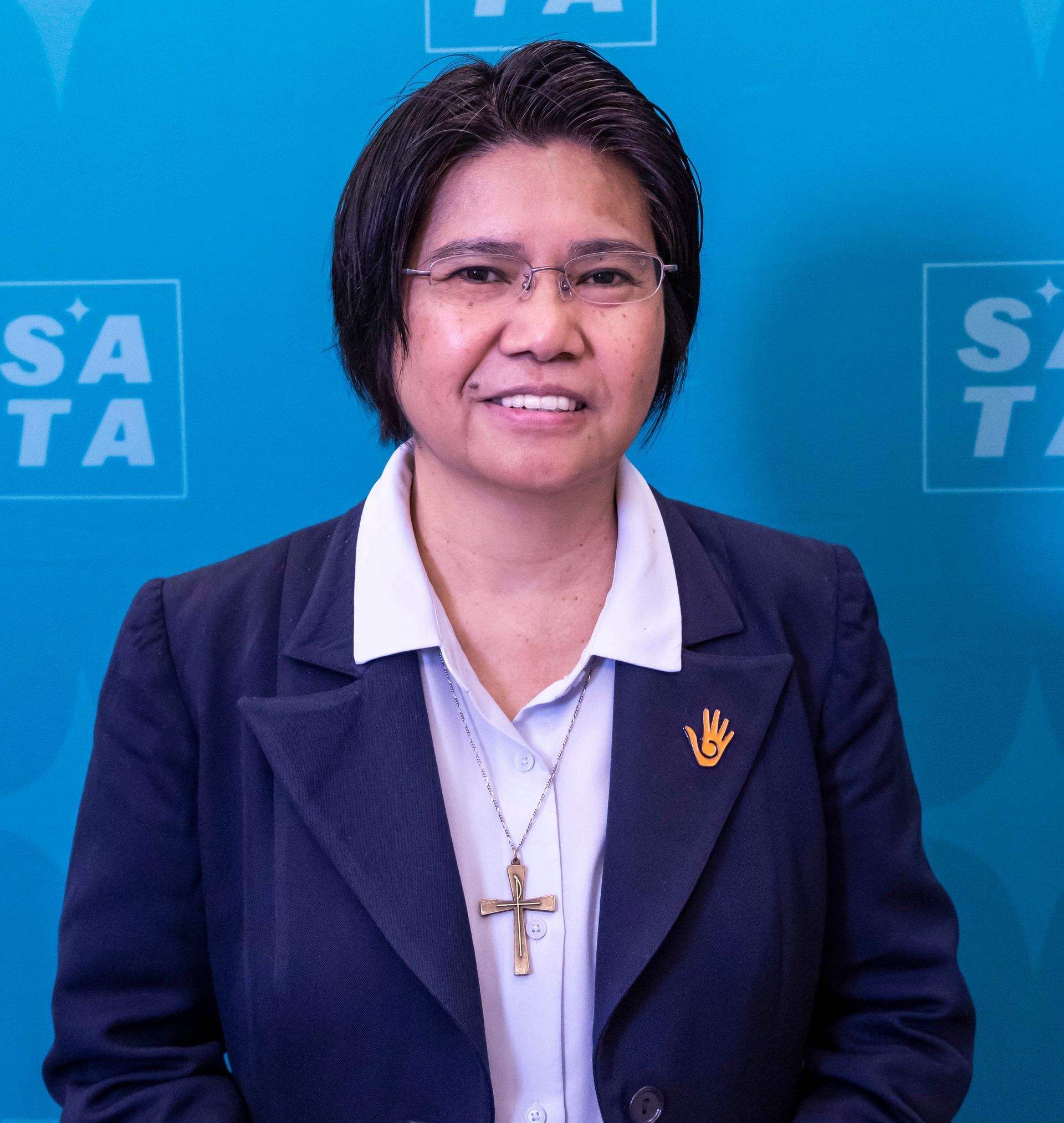 Smiling Black woman in purple dress, curly hair, holding a framed document outdoors.