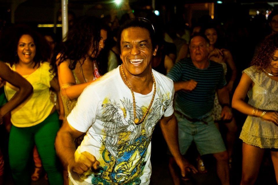 Man dancing, smiling at a party at night. Crowd in background.