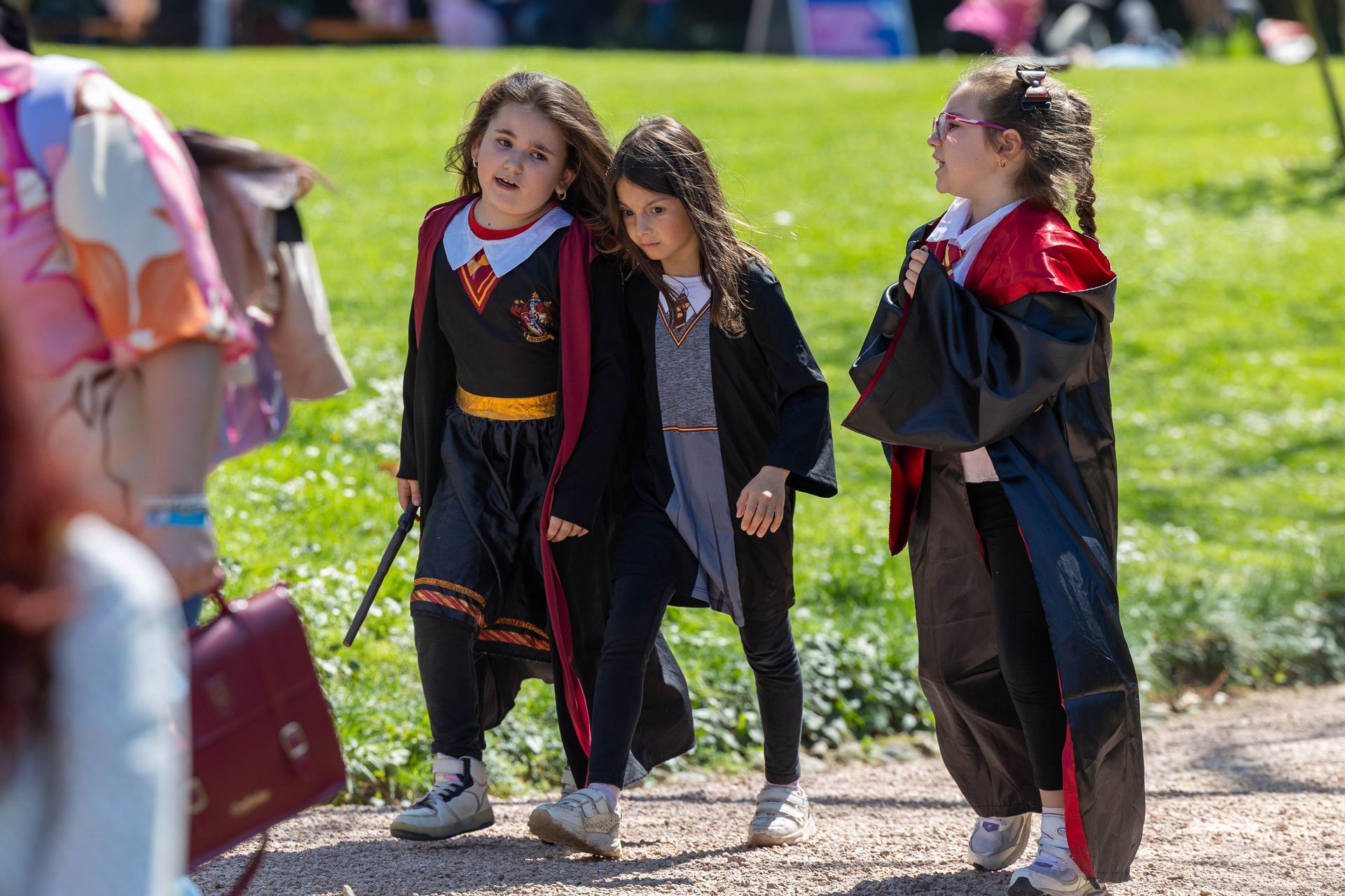 Tre bambini vestiti con tuniche a tema Harry Potter camminano insieme su un sentiero soleggiato all'aperto.