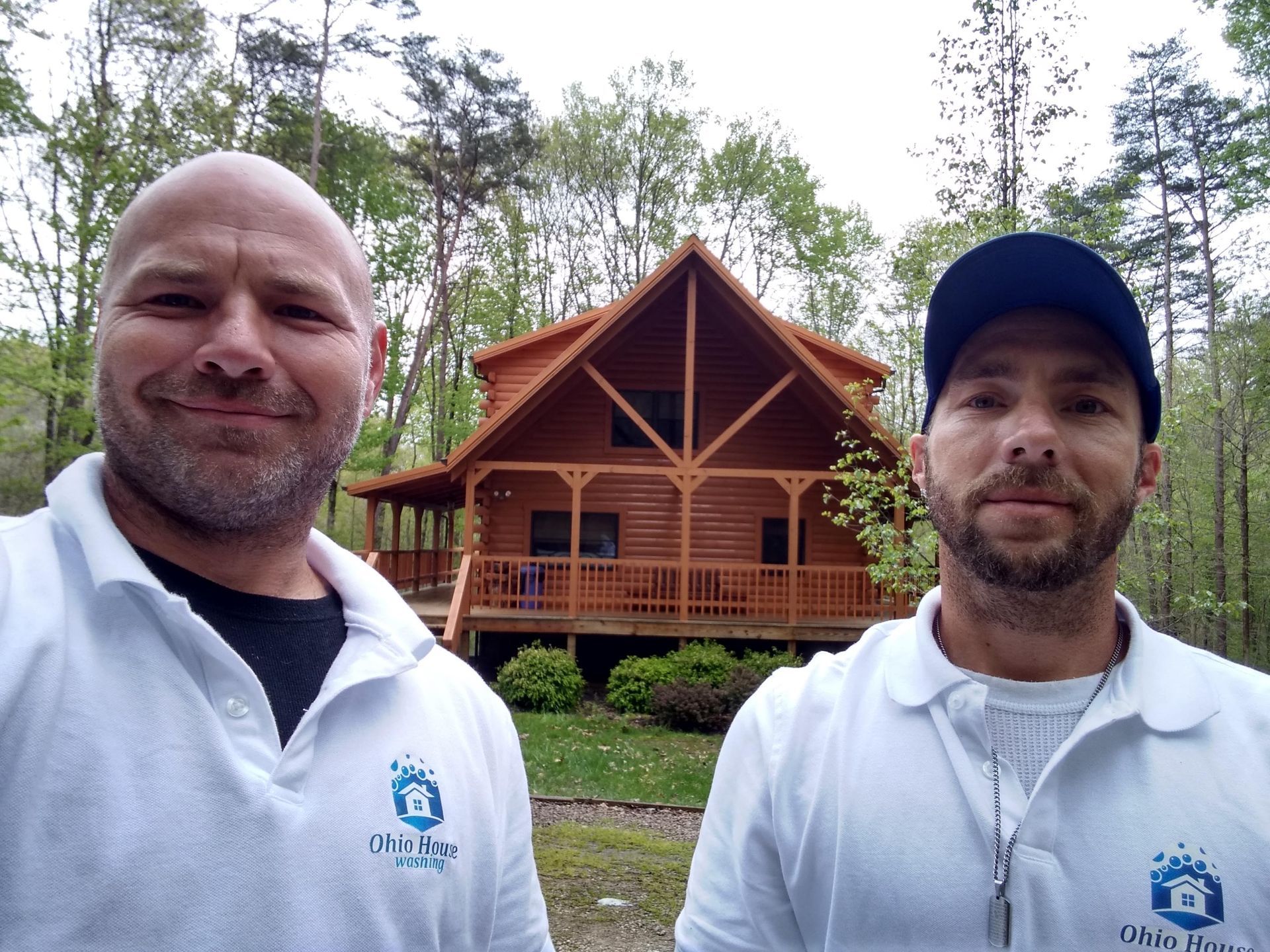 Person power washing the gray siding of a house with a white window on a sunny day.