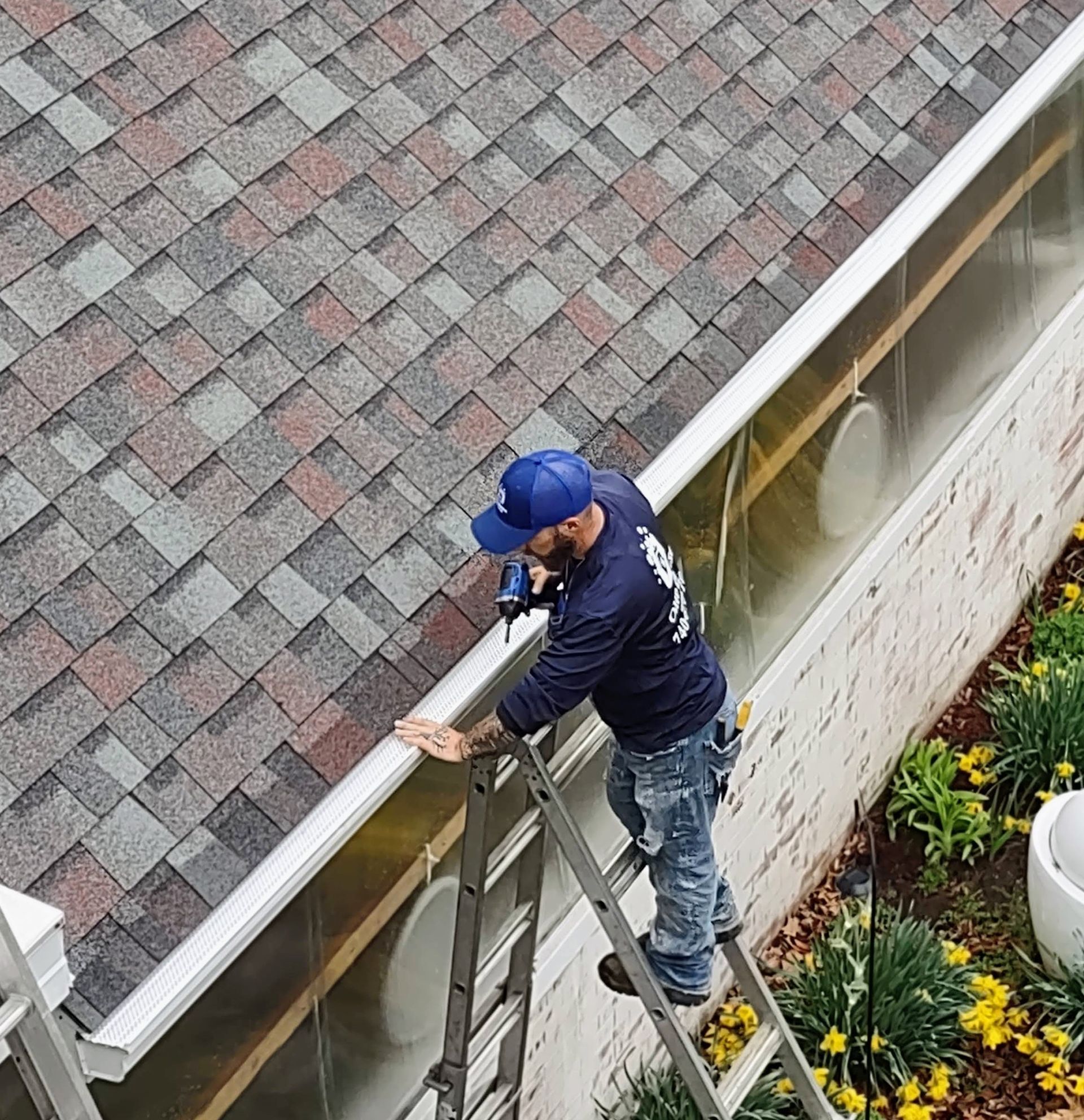 Person in orange glove cleaning a gutter filled with leaves and debris from a roof.