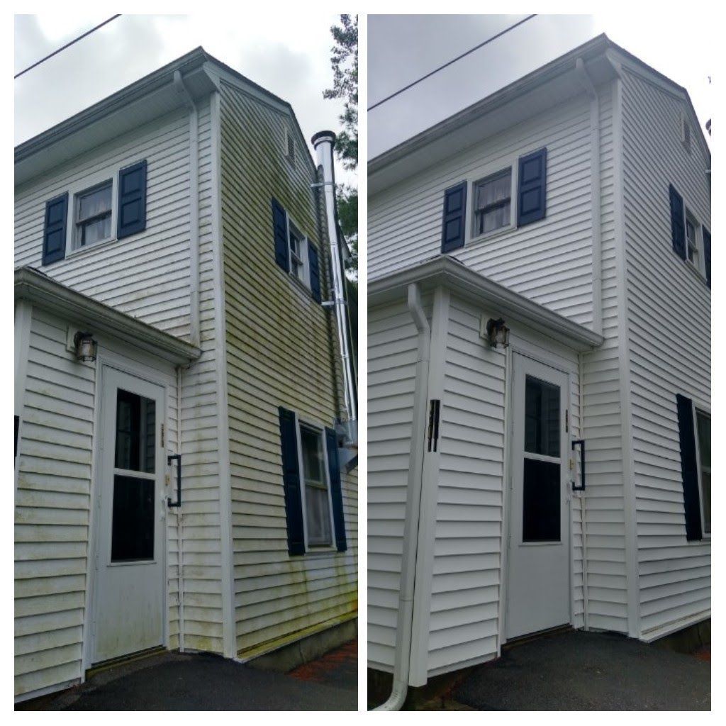 Person power washing the side of a light-colored house with black shutters, from a wooden deck.