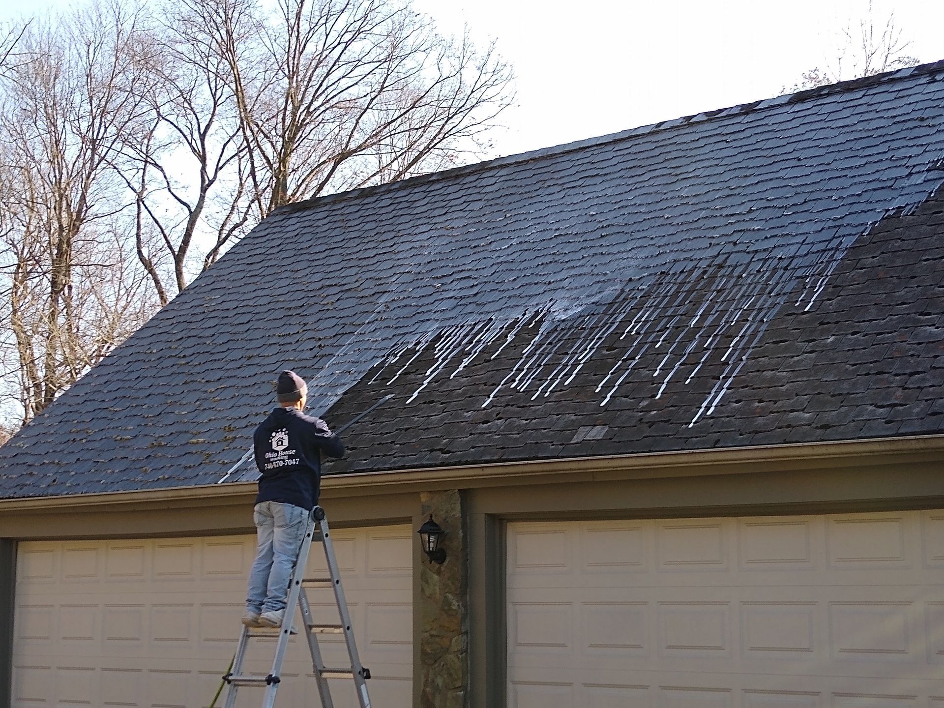 Man power washing a metal roof with a high-pressure hose, sunny day.