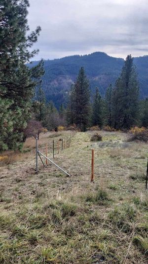 There is a fence in the middle of a field with mountains in the background.