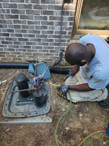 A person working on an outdoor air conditioning unit next to a brick wall.