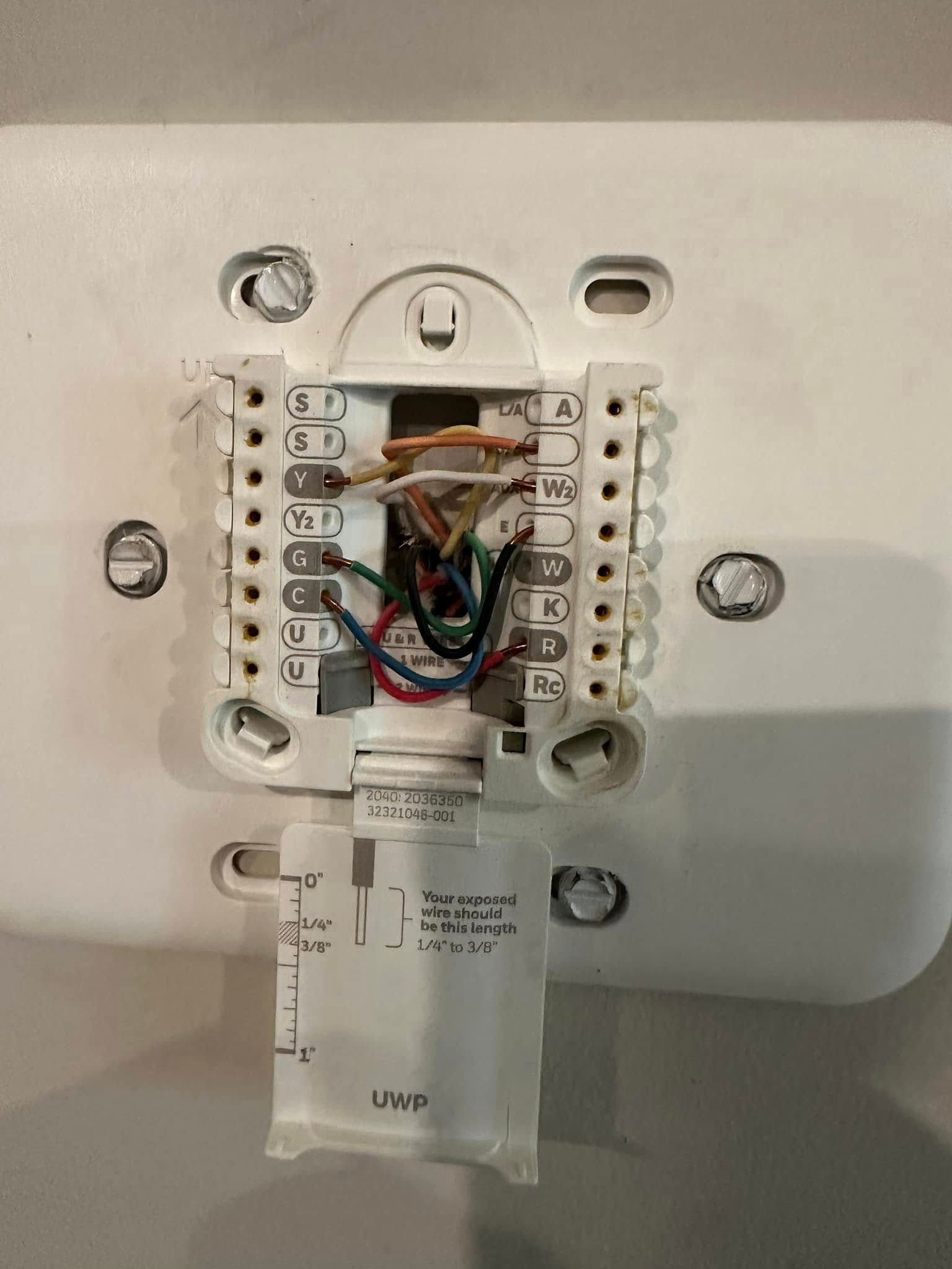 HVAC technician working on an outdoor air conditioning unit. Brick wall, ground.