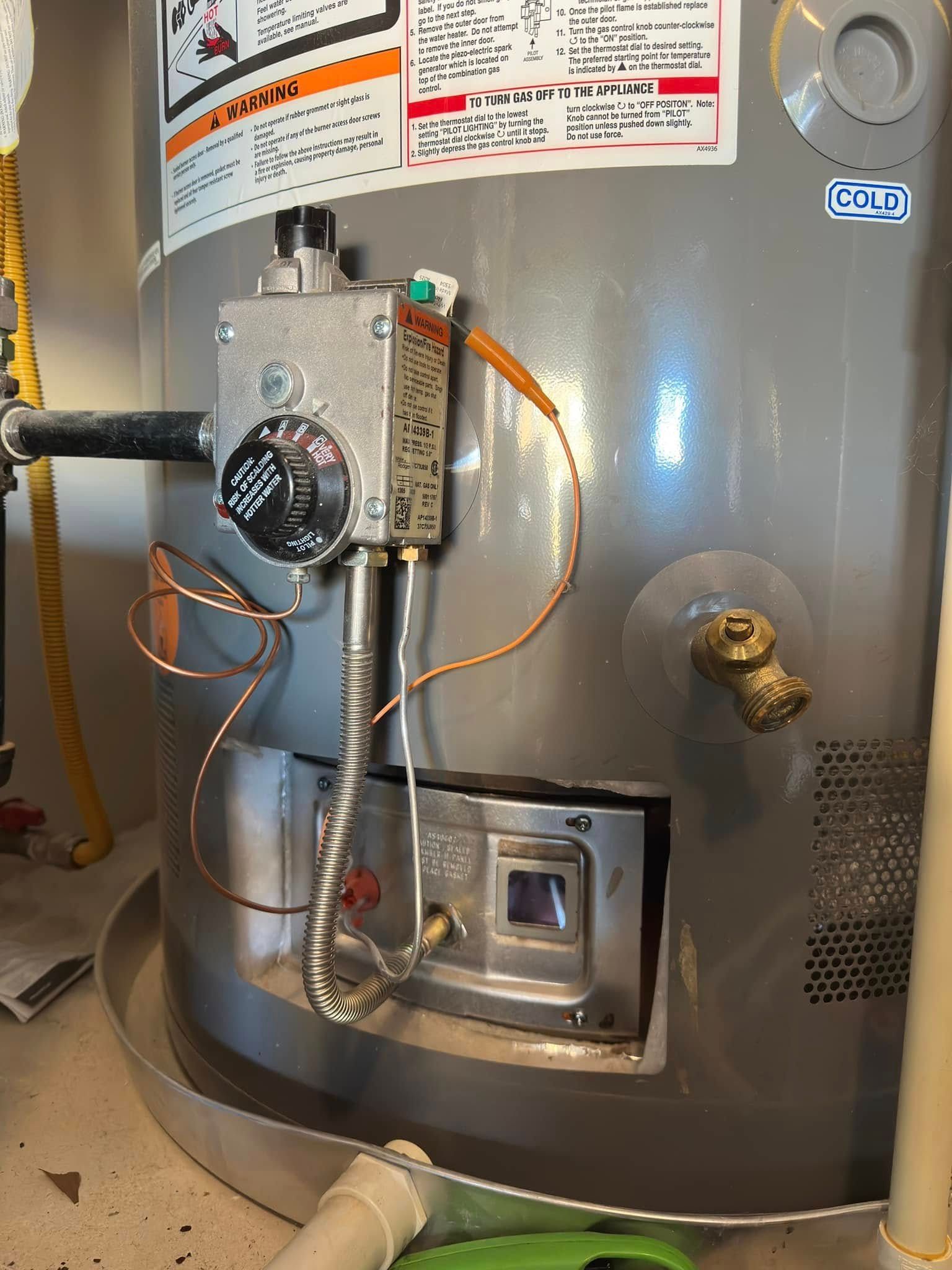 A close-up of a gray water heater with visible temperature controls and gas valve.