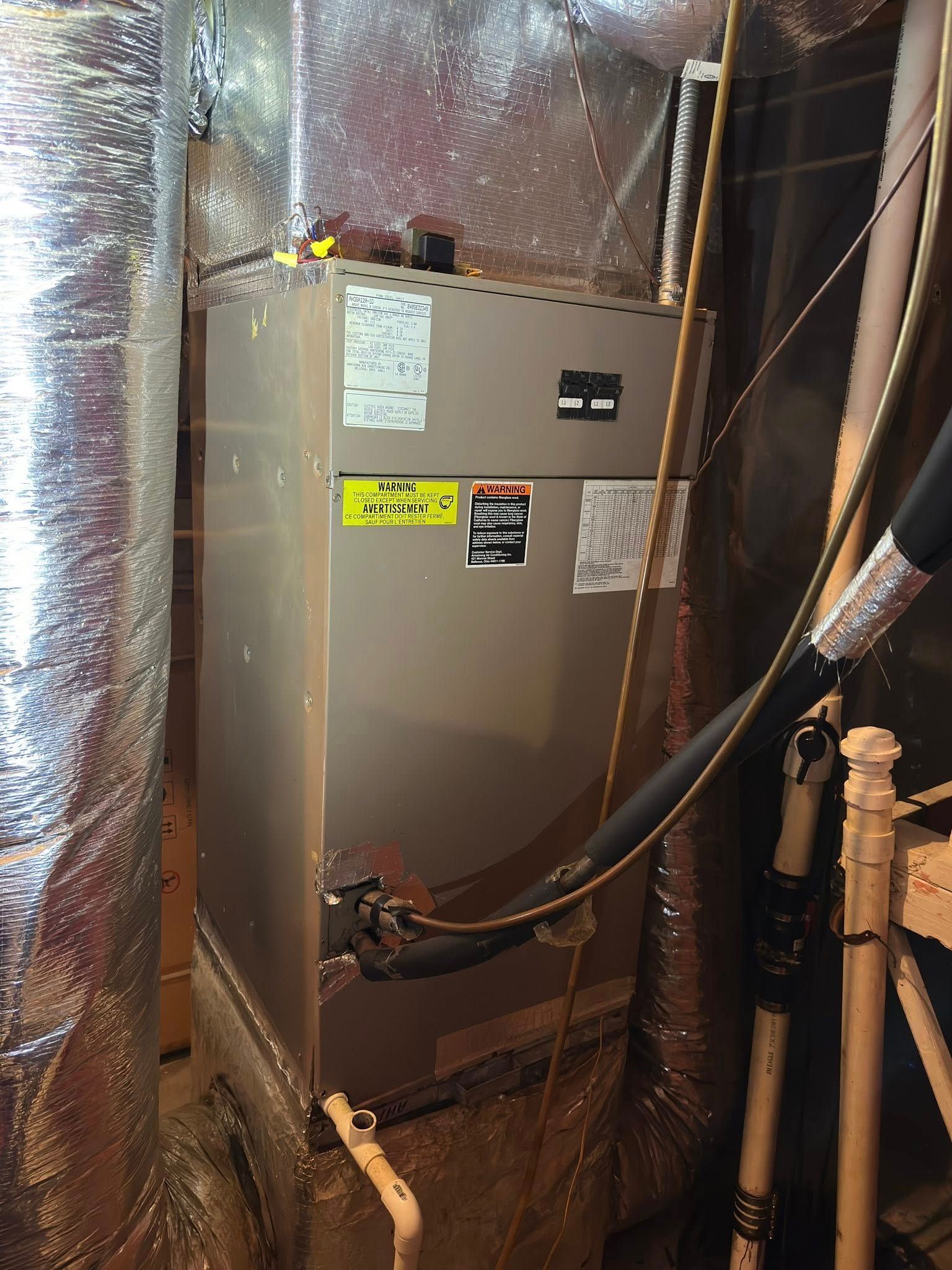 Furnace unit in a basement, wrapped in silver insulation, with various pipes and vents.