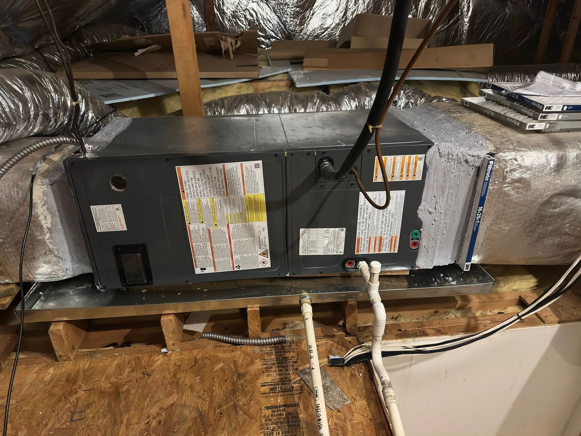 HVAC unit in attic, gray metal box, ductwork, insulation, wooden structure.