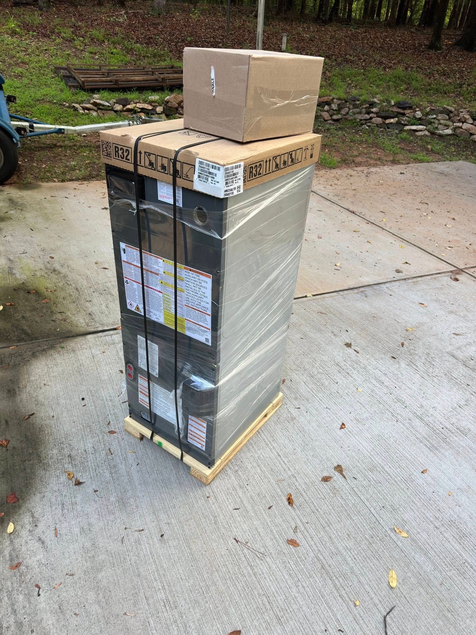 A tall, wrapped package on a pallet outdoors, with a smaller box on top.