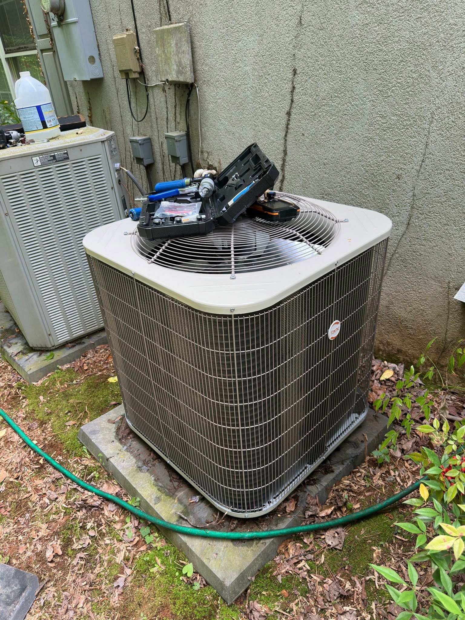 Air conditioning unit with open top and exposed components, outdoors near a building.