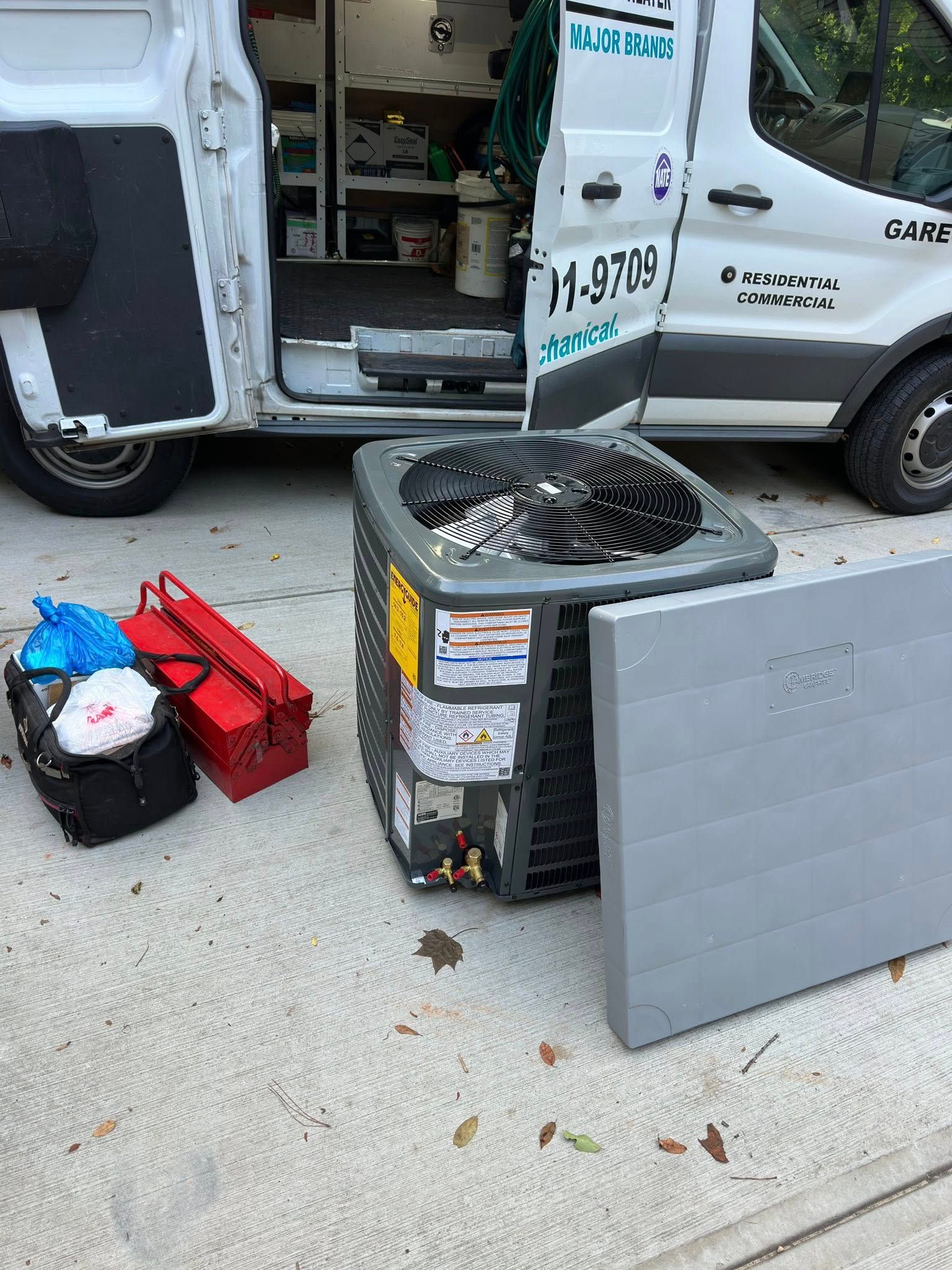 Air conditioner unit with open access panel, next to a service van with open door and tools.