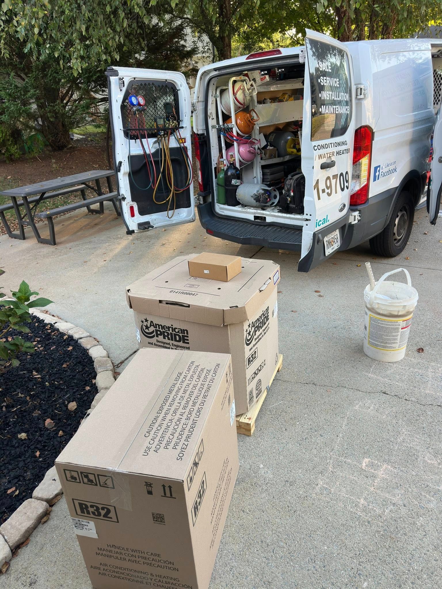 Two cardboard boxes on pallets in driveway near a white van with open doors.