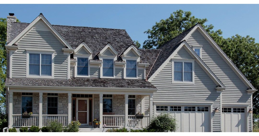 Two-story gray house with front porch, gabled roof, and two-car garage under a blue sky.