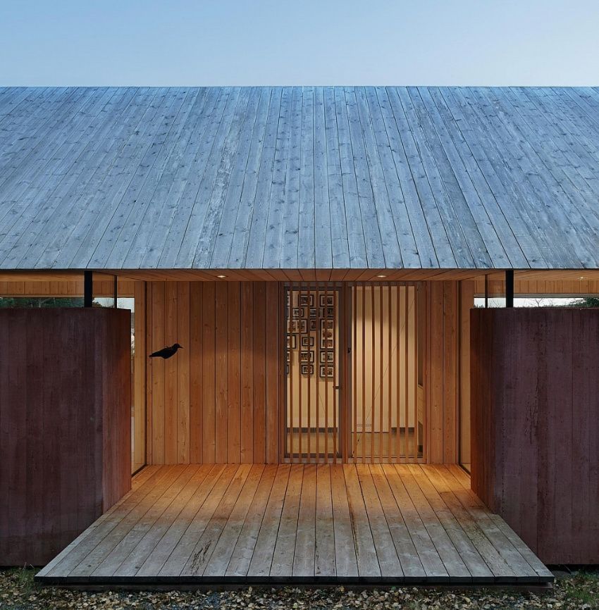 Wooden entrance of a building with a large wooden roof, two rusty-brown walls, and a bird silhouette.