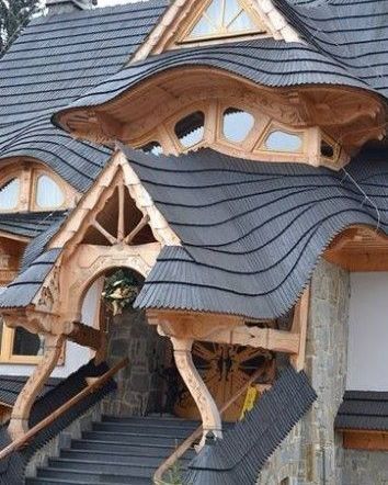 Ornate wooden entrance to a building with wavy, dark grey roof and stone facade.