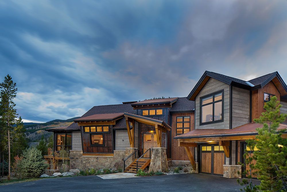 Rustic mountain home with stone, wood, and metal exterior, under a cloudy twilight sky.