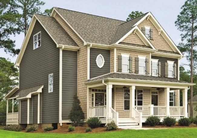 Two-story house with tan and gray siding, porch, and brown roof.