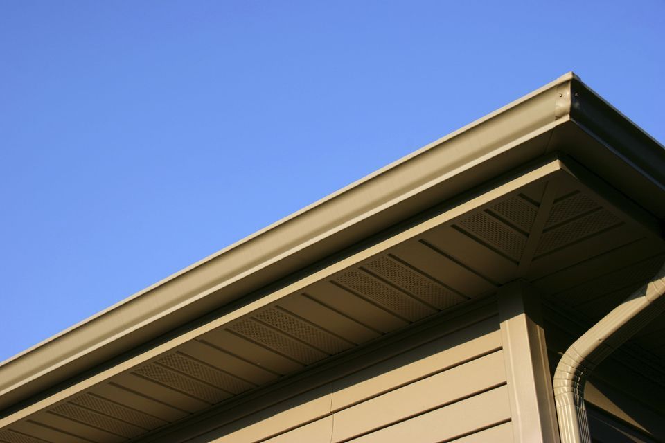 Beige house siding and dark-brown gutters against a blue sky.