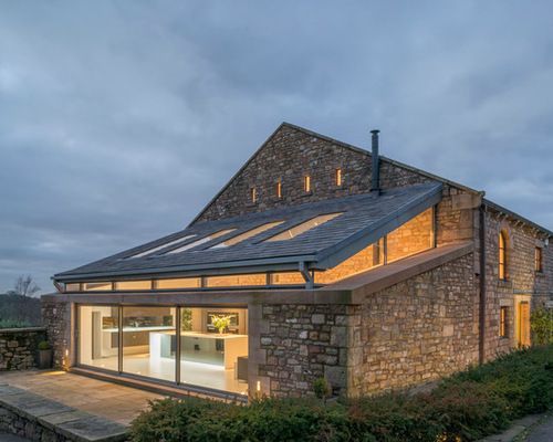 Stone building with a modern glass extension lit at dusk.