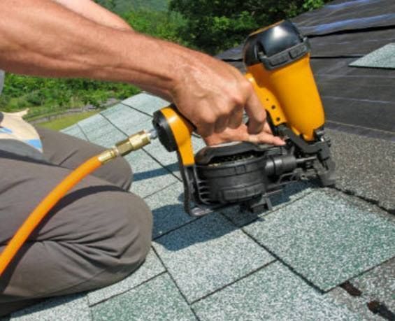 Person using a yellow nail gun to fasten shingles on a roof.
