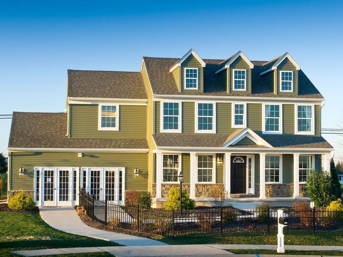 Green two-story house with white trim, dormers, and stone accents, blue sky.