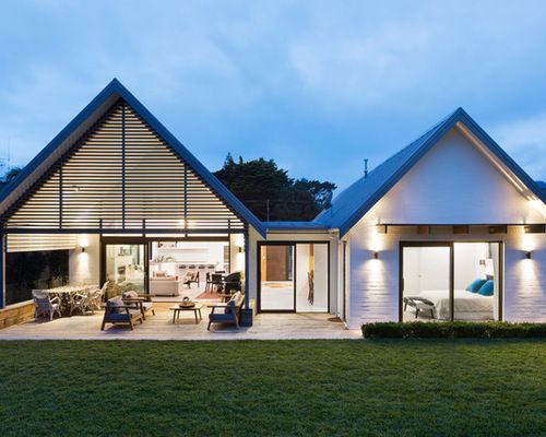 Modern white house with open-plan living and a lawn, patio, and glass doors. Evening setting.