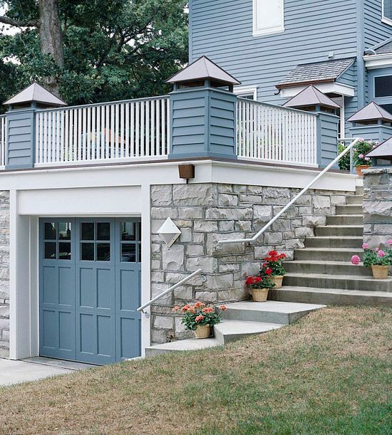 Garage with blue door, stone facade, deck with white railing, and exterior staircase.