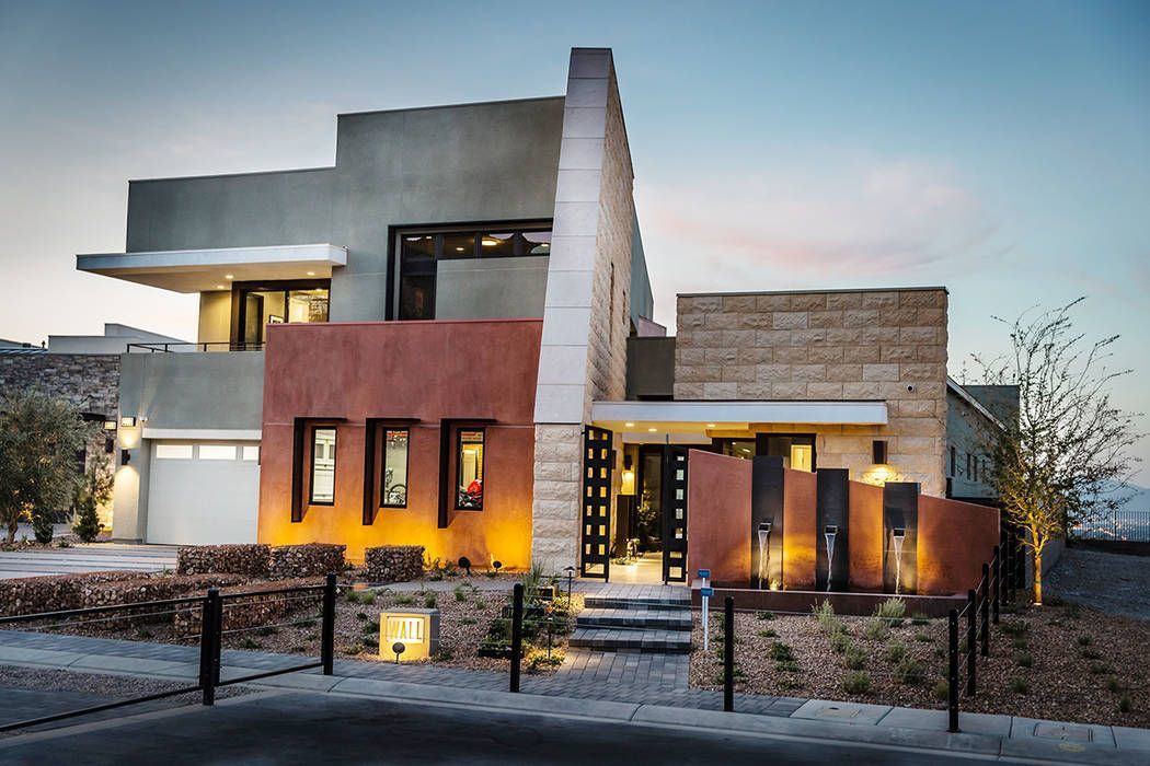 Modern two-story house with varied stone and stucco facade, featuring a water feature and lit landscaping.