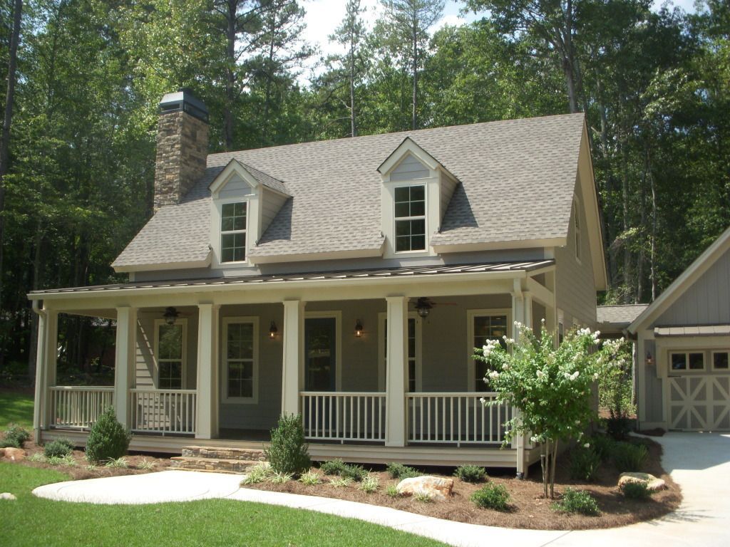 Cottage-style home with porch, dormers, and stone chimney. Landscaped yard, attached garage, trees in the background.