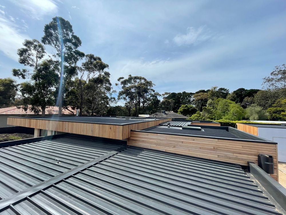 Gray metal roof with wooden trim, sunny sky, trees in the background.