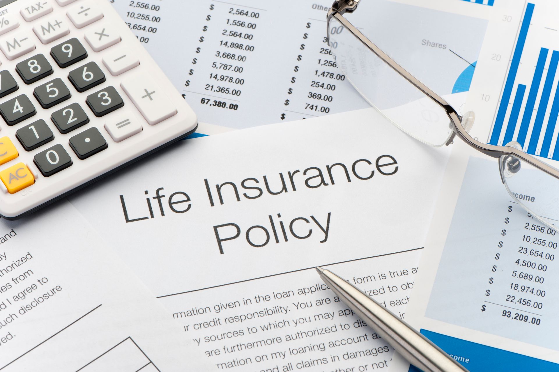 A life insurance policy is sitting on a table next to a calculator and glasses.
