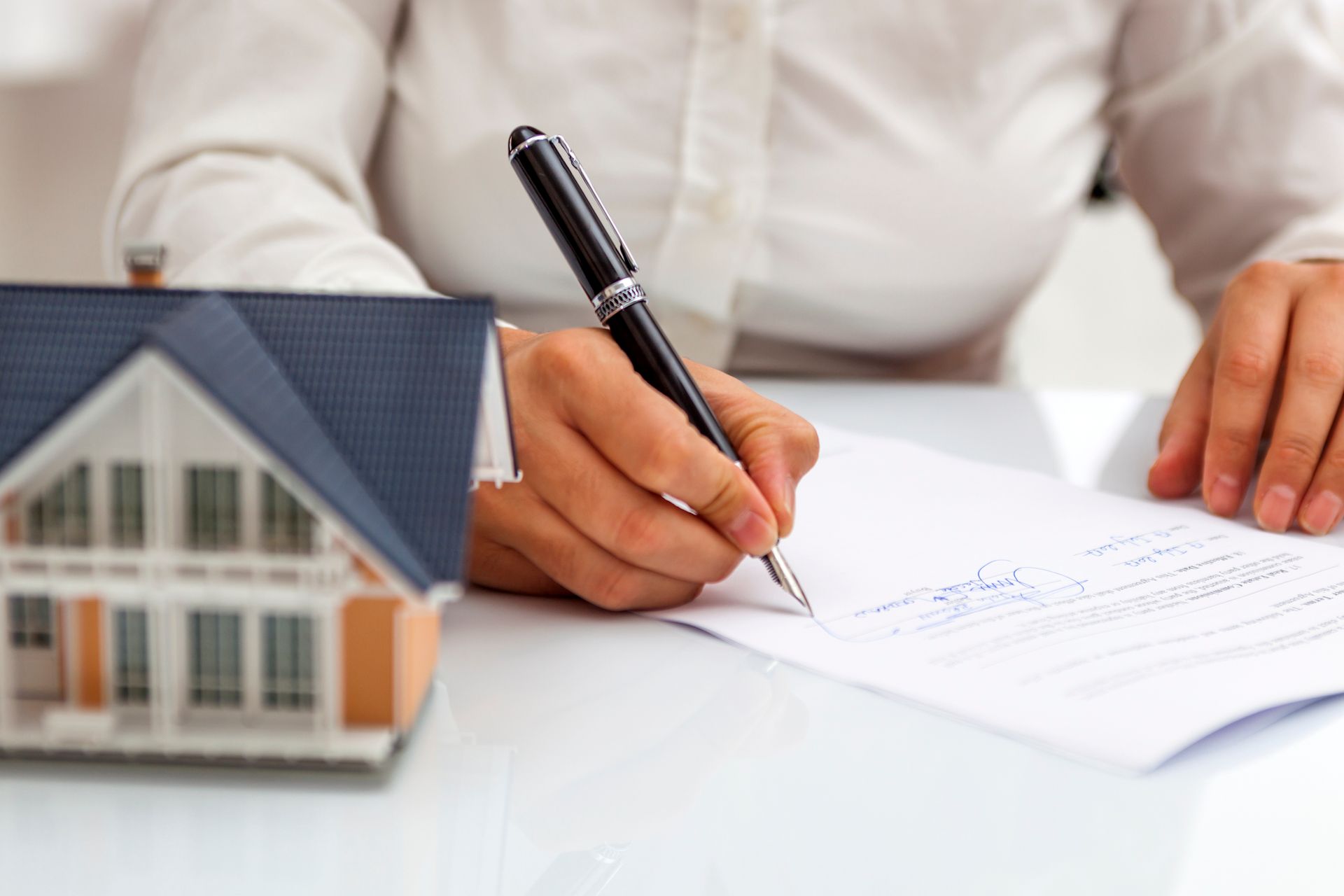 A woman is writing on a piece of paper next to a model house.
