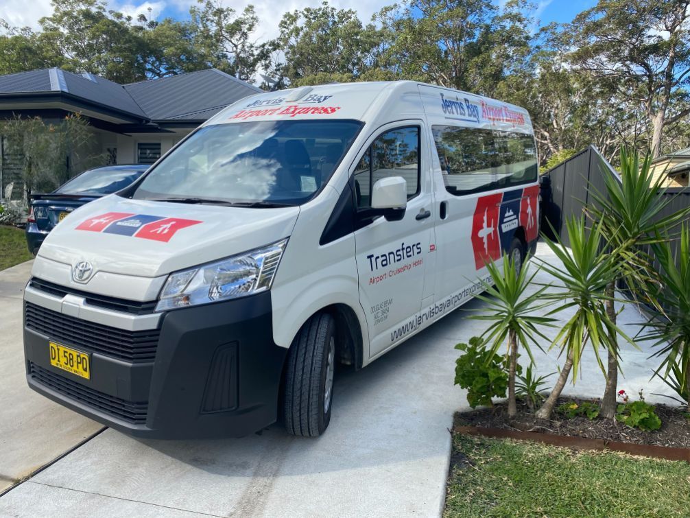 A White Van Is Driving Down A Road With Mountains In The Background — Jervis Bay Airport Express In Swanhaven, NSW