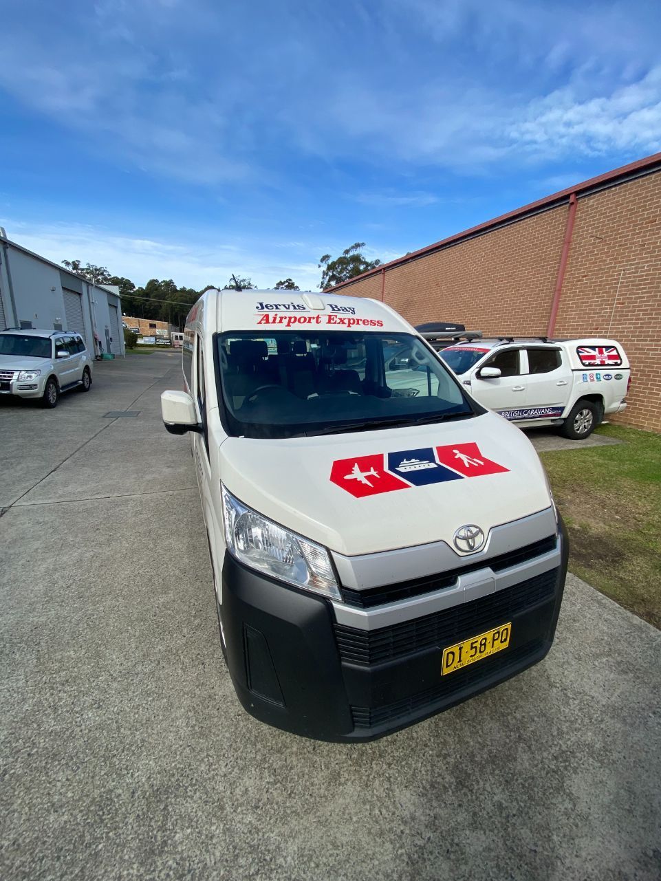 A White Van Is Parked In A Parking Lot Next To A Bus — Jervis Bay Airport Express In Ulladulla, NSW