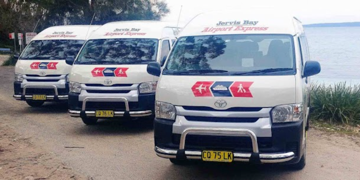 Three Jervis Bay Airport Express shuttle vans parked near the shoreline