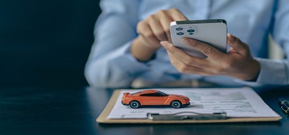 A person is holding a cell phone in front of a toy car on a clipboard.