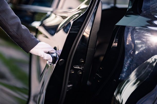 A man in a suit is opening the door of a black car.