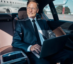 A man in a suit is sitting in the back seat of a car using a laptop computer.