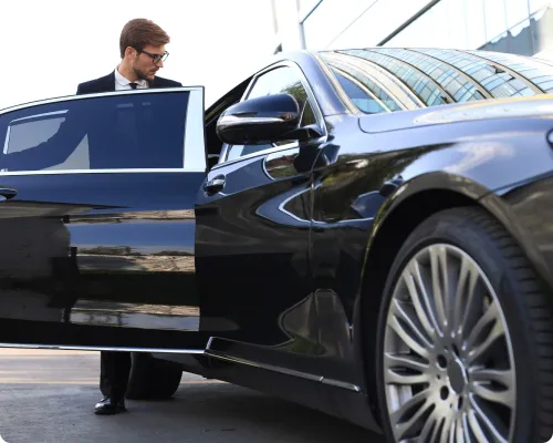 A man in a suit and tie is getting out of a black car