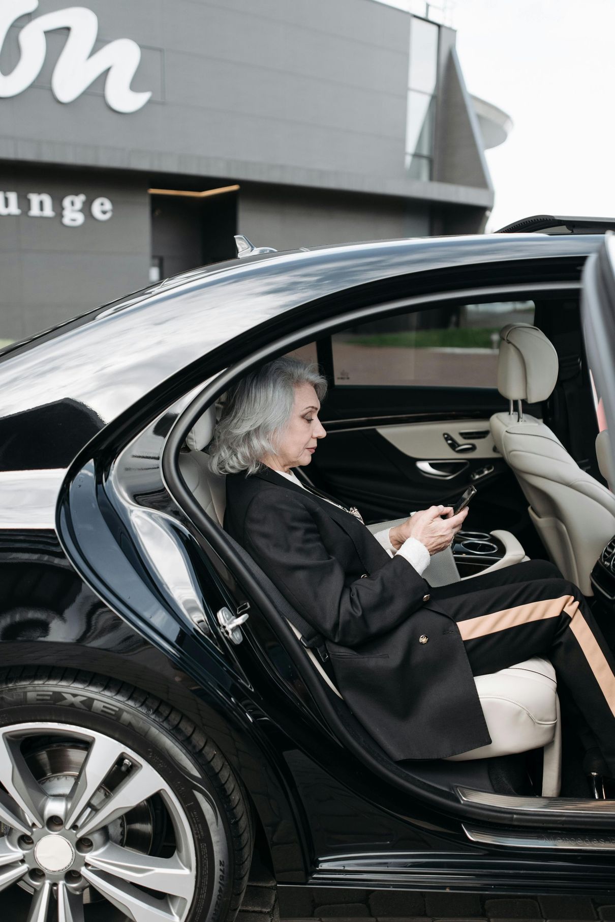 A woman is sitting in the back seat of a car looking at her phone.