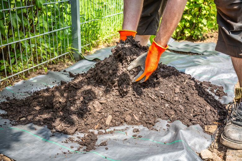 A man wearing orange gloves is spreading dirt on a tarp.