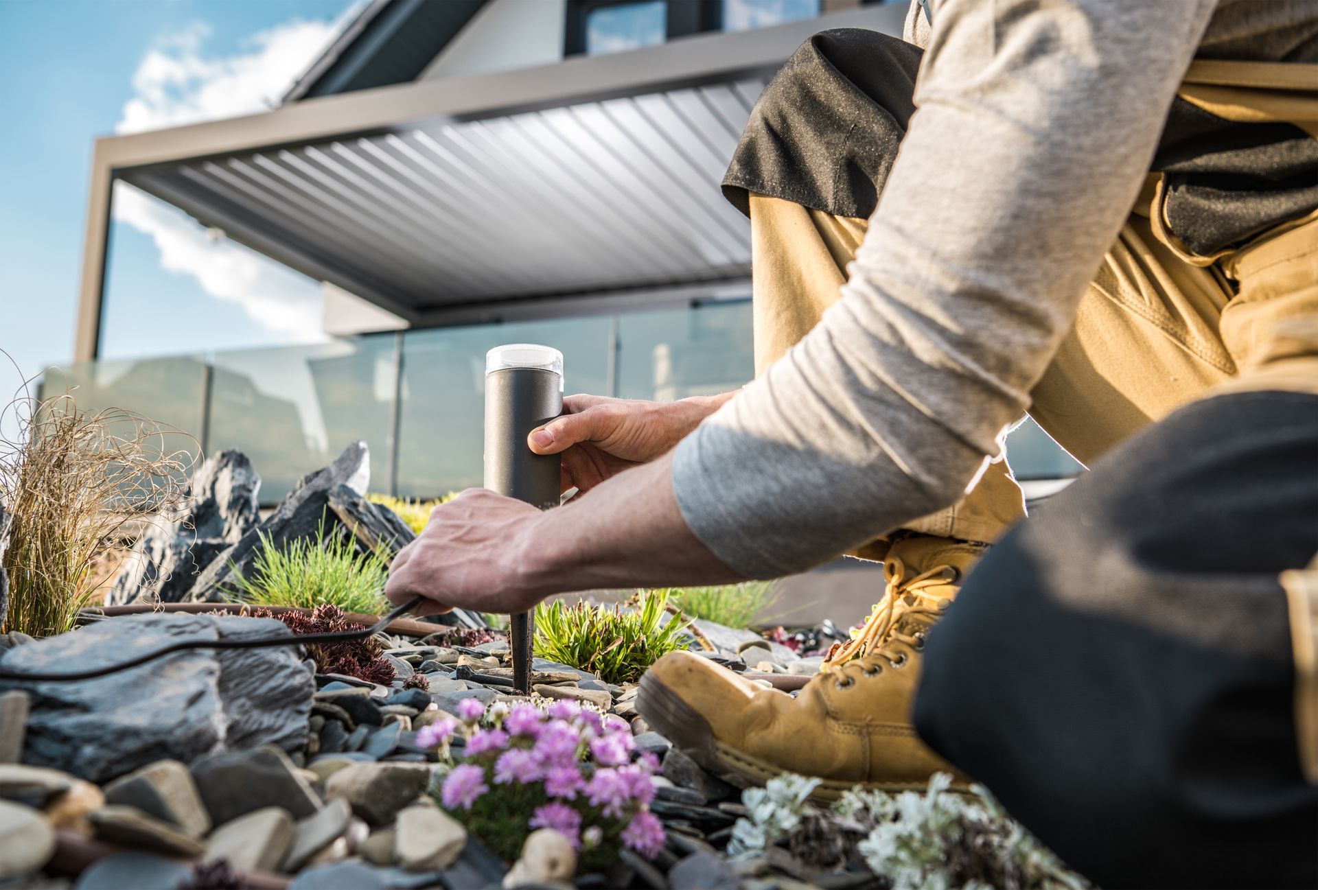 A man is working in a garden in front of a house to install lights.