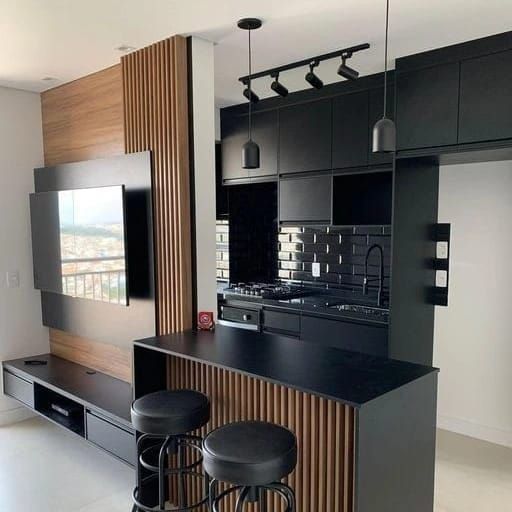Una cocina con gabinetes y taburetes negros y un televisor de pantalla plana en la pared.