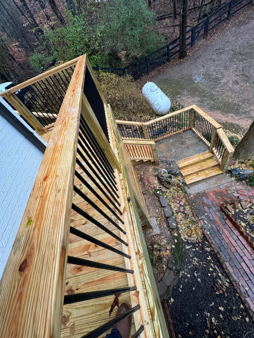 A high-angle view of a newly built wooden deck with black railings overlooking a backyard with stone stairs and a patio.