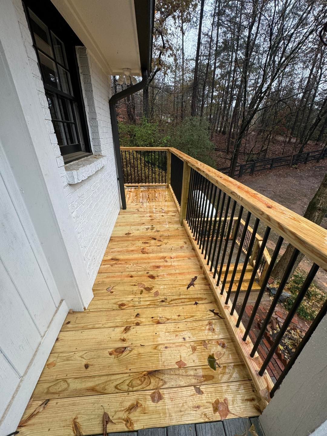 A newly constructed wooden deck featuring light-colored planks, a wooden top rail, and black metal vertical balusters.