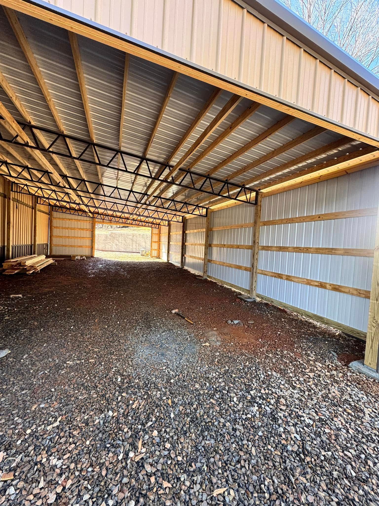 A view inside an open-walled metal pole barn with wooden support beams and a gravel floor.