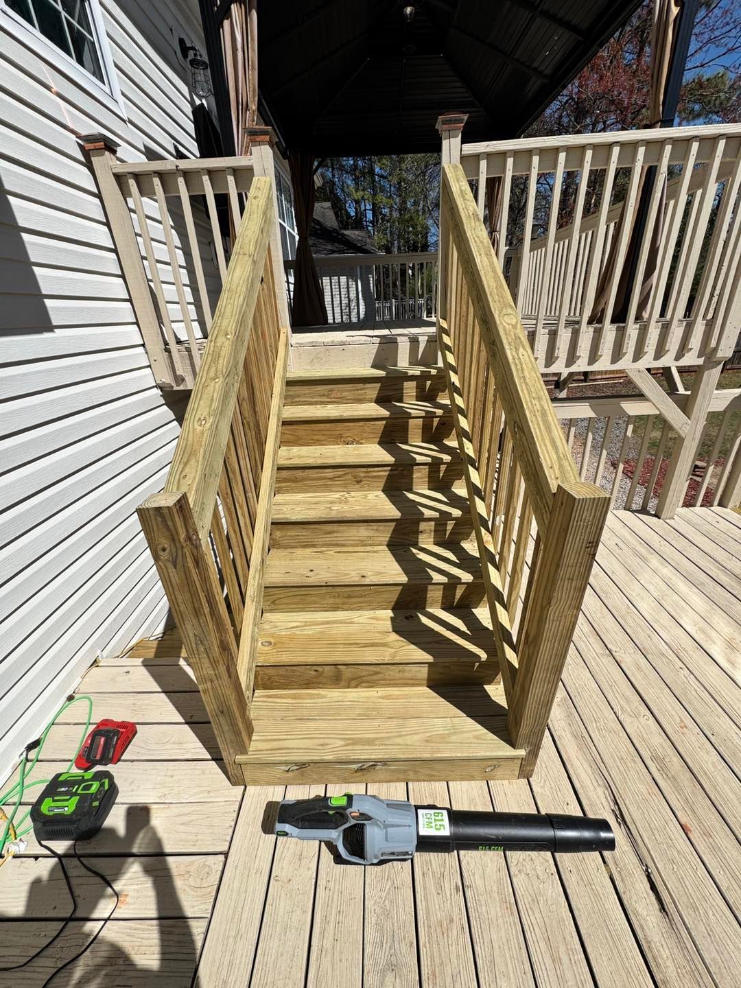 Newly constructed wooden staircase leading up to a deck, with a leaf blower placed on the deck surface in the foreground.