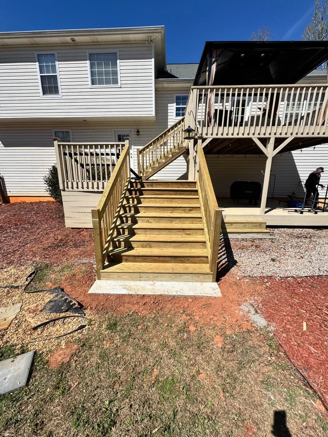 A two-story house with light siding featuring a new wooden staircase leading up to an elevated deck and a lower porch.