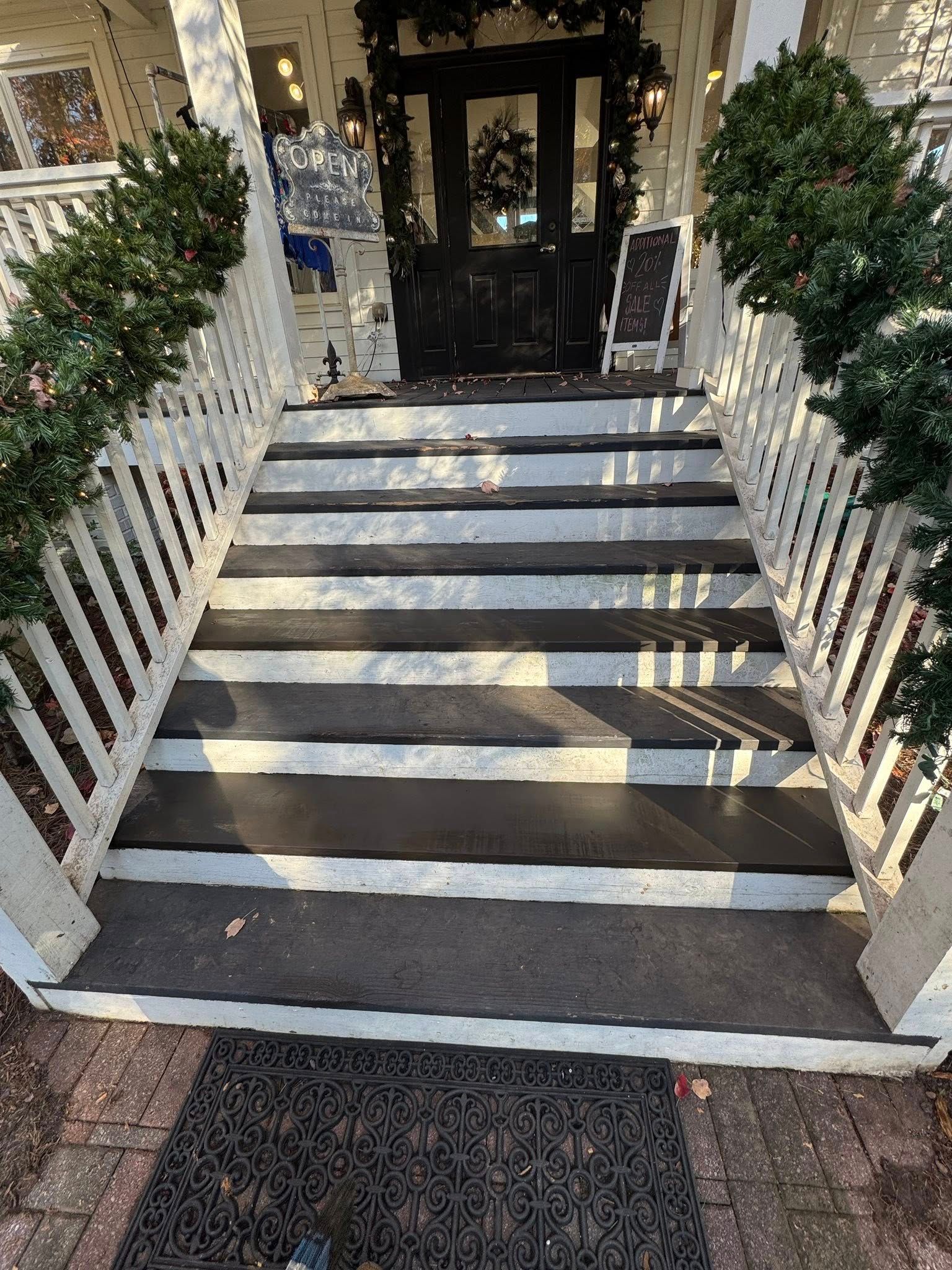A set of exterior wooden stairs painted with black and white horizontal stripes, flanked by white railings and greenery.
